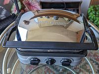 Top view of Cuisinart Griddler showing chrome lid with black handle and brand name on surface.