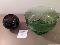 Two glass items side by side on a surface: a green textured bowl with hexagonal base and a smaller purple honeycomb vase.