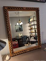 Front view of large rectangular wood-framed mirror with twisted rope design and brass rods showing reflection of room interior.