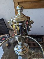 Full front view of large chrome-plated ceramic urn with lid and decorative finial, showing shape and reflective surface.