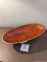 Front view of large oval aluminium bowl showing textured orange interior and polished exterior edges.