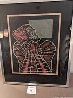Framed print showing abstract bound figure in red and black tones with a green square on a black background.