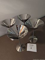 Four stainless steel martini stemware glasses arranged together showing polished inner surfaces and brushed stainless outer surfaces.
