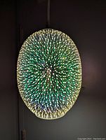 Front view of illuminated light shade showing detailed 3D starburst effect with green and yellow tones.