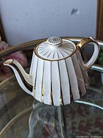 Side view showing the ribbed cream body with gold stripes and handle with gold accent.