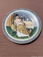 Full image of round ceramic plate with center painted scene of a seated woman in western-style attire, chair, table with flowers and mirror, and a small dog on carpet.