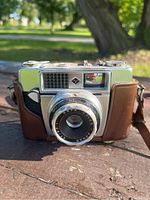 Front view of Agfamatic Ia camera showing lens, rangefinder window, and part of the leather case.