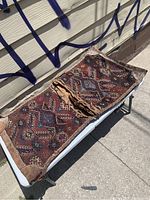 Two antique Persian hand knotted saddle bags laid out on a table, showing overall size and condition with visible wear and some damage.