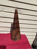 Moose call standing upright against a white background on red fabric, showing conical shape and decorated birchbark material.
