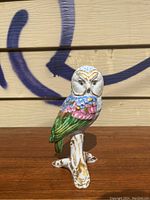Front view of the porcelain owl figurine on wooden surface with graffiti background, showing the full figure perched on branch.