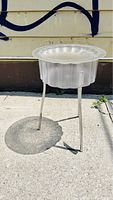 Photo of the clear acrylic flower-shaped side table with metal legs placed outdoors on pavement, showing side profile and top surface.
