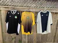 Front view of three soccer jerseys on hangers: first black Umbro Ireland International, second yellow-black Nike Glasgow Celtic, third black-gray Adidas Newcastle United.