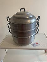 Front view of three-tier pagoda style metal steamer with lid and handles.