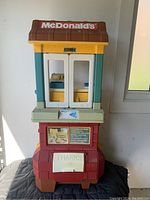 Front view of the McDonald's branded child's play restaurant toy station showing overall structure, roof with logo, double doors, and lower compartment.
