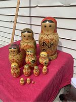 Full view of the set of 13 nesting Babushka dolls arranged in graduated order on red cloth with a ruler in the background showing size of largest doll around 13 inches