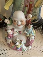 Front and partial side view of a ceramic smiling Buddha figure with six children, showcasing detailed colorful hand painting and facial expressions, on a wooden base.