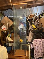 Front view of the tall standing vitrine display cabinet with steel and wood frame and glass shelves, surrounded by miscellaneous items.