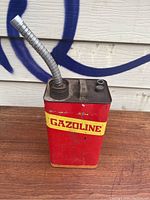 Full view of vintage red gasoline can with yellow label and flexible metal pouring spout attached