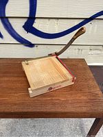 Front view of the wooden Ingento guillotine cutter showing the cutting surface and blade arm on a wooden table.