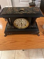Front view of antique black mantel clock with speckled gold detailing, Roman numeral clock face, and winding key on top