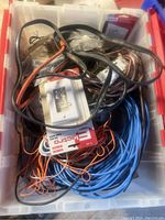 Top down view of storage tote containing assorted electrical wires, dimmer switches with wall plates, various cables in black, orange, and blue, and packaged speaker wire.