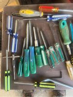 Assorted screwdrivers with various colored handles - green, blue, yellow, orange. Mixed types including flat and Philips heads.