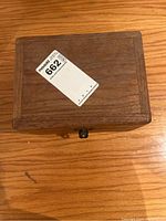 Closed photo of the wooden case housing brass weights, showing wood grain and metal clasp.