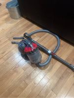 Full view of Dyson canister vacuum on hardwood floor showing hose, wand, and cyclone dust bin.