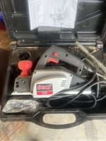 Freud FE82 portable electric planer inside black carrying case with power cord and red adjustment knob accessory. Spare parts list also inside the case.