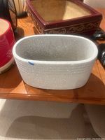 Photo of multiple planters including a white oval planter with a visible chip and a square red and gold planter, on a wooden table surface.