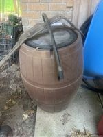Brown plastic rain barrel with a screen top, showing the barrel's exterior and the long drain hose resting on top.