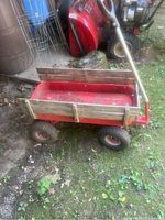 Side view of red metal wagon with wood rails, pneumatic tires, and metal handle, showing condition and features.