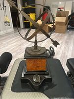 Decorative armillary sphere sundial with an arrow gnomon, mounted on a decorative pedestal base with magnifying glass detail.