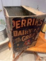 Top and side view of vintage rectangular metal box with dairy advertising graphics showing wear and edge damage
