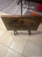 Photo of vintage folding TV table showing top with countryside scene and foldable legs.