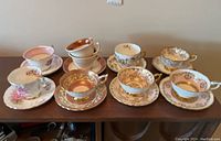 Overview photo of 8 vintage china teacups and saucers with various floral and gold designs, displaying general condition and style