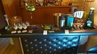 Overview of barware lot on black padded surface including decanter, glasses, bar tools, ice buckets, and accessories.