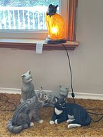 Cat lamp illuminated on wood base with translucent orange textured body and black cat head near window.
