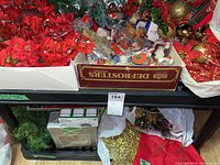Box with red fabric tree skirt partially visible, green garland and more faux floral bunches on a shelf