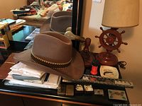 Brown felt cowboy hat with woven band on a dresser with other items visible