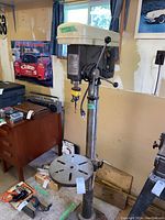 Full view of the Power Maxx drill press showing its pedestal, adjustable table, and motor assembly in a workshop setting.