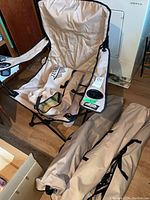 Photo of one unfolded beige Tera Gear folding chair with cup holder in right armrest and a matching carrying bag beside it showing chair's fabric seat and backrest.