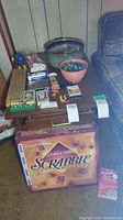 Full lot overview photo of Scrabble Deluxe Edition box, cribbage board box, bowls of marbles, playing cards, poker chips, whistle, and puzzles on table and floor