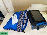 View of Garmin GPS unit on top of a black and blue zippered case and its box alongside a blue zippered pouch with mounting accessories visible inside.