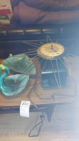 Photo of two turquoise-blue leaf-shaped ceramic dishes, MCM starburst wall clock with gold spokes, and vintage black radio with tuning dial and knobs on a table.