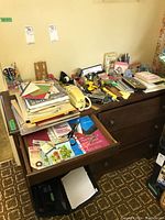 Top and drawer views showing various office supplies including staplers, tape holders, calculators, telephone, folders, and stationery organized on and inside a wooden dresser.