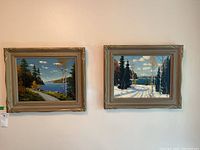 Both framed paintings hung on wall showing colorful autumn and winter landscapes by C.C. Milne.