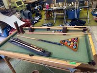 Full view of the portable pool table including billiard balls in wooden rack and multiple pool cues laid out on the table.