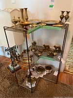 Front and side view of the metal corner shelving unit showing overall structure including 3 shelves with lattice base and dark metal frame. Green protective tape on top shelf edges visible. Unit is placed indoors on carpet.