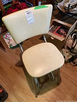Front angled view of vintage stool showing cream vinyl cushioned seat and backrest with chrome frame